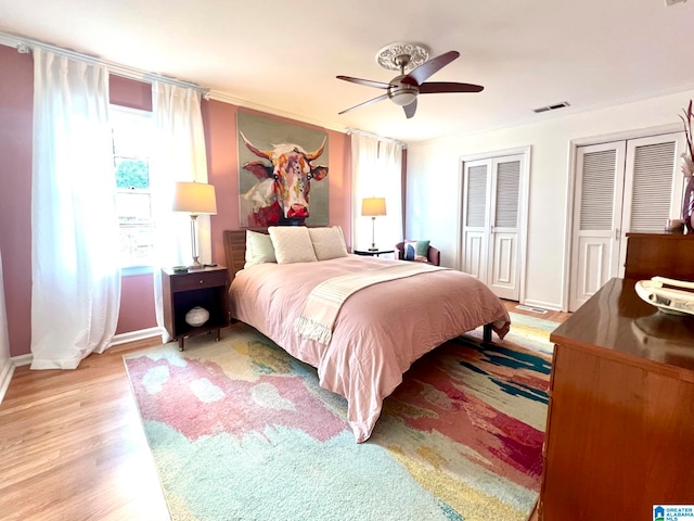 bedroom with ceiling fan, multiple closets, and light hardwood / wood-style flooring