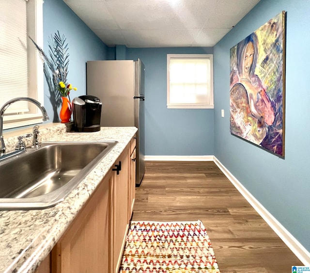 kitchen with hardwood / wood-style flooring, stainless steel fridge, light stone counters, and sink