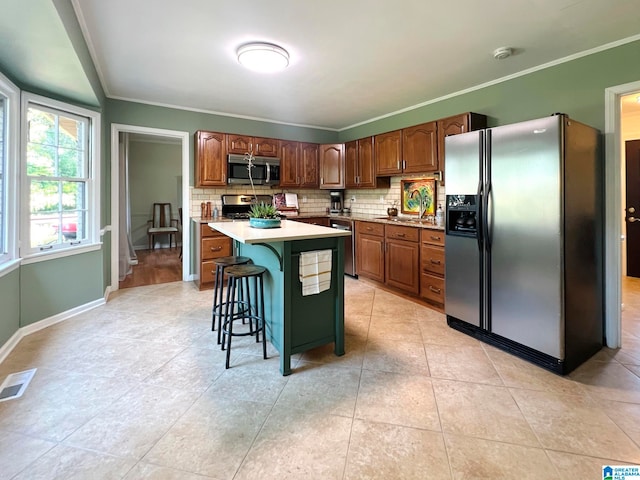 kitchen with crown molding, a breakfast bar area, decorative backsplash, a kitchen island, and appliances with stainless steel finishes