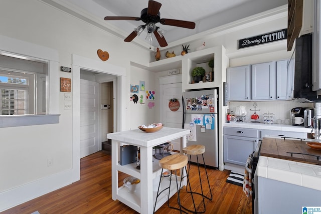 kitchen featuring gray cabinetry, dark hardwood / wood-style flooring, tile counters, and stainless steel refrigerator