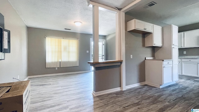 kitchen with white cabinets, wood-type flooring, and a textured ceiling