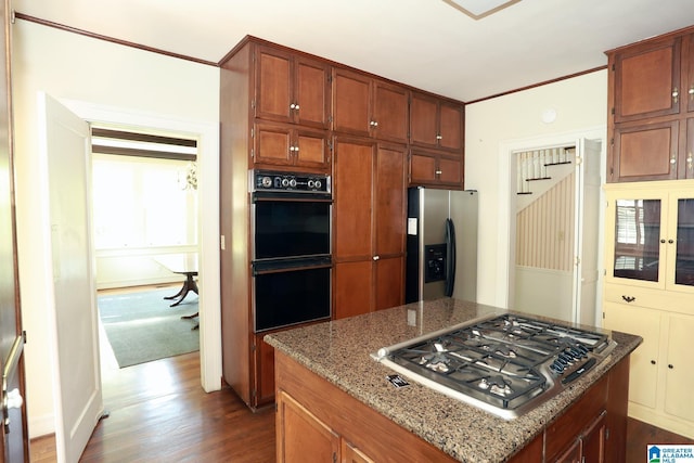 kitchen featuring light stone countertops, a center island, stainless steel appliances, dark hardwood / wood-style flooring, and crown molding