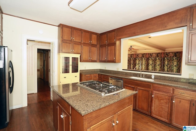 kitchen with appliances with stainless steel finishes, dark stone counters, dark wood-type flooring, sink, and a center island