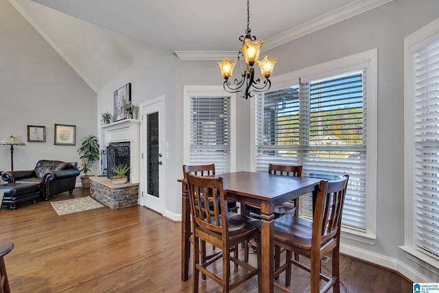 dining space featuring hardwood / wood-style floors, a notable chandelier, a fireplace, and vaulted ceiling