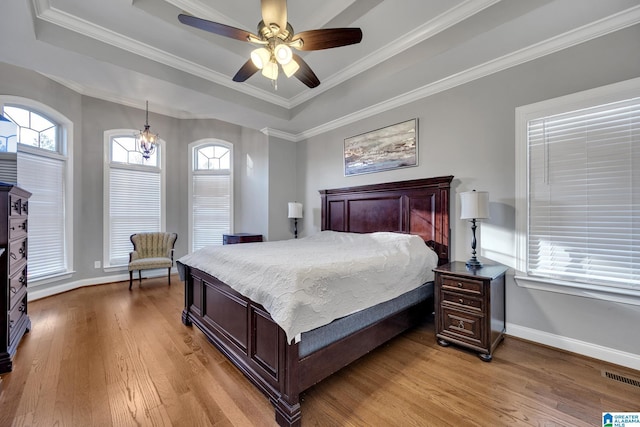 bedroom featuring a raised ceiling, crown molding, light hardwood / wood-style flooring, and ceiling fan with notable chandelier