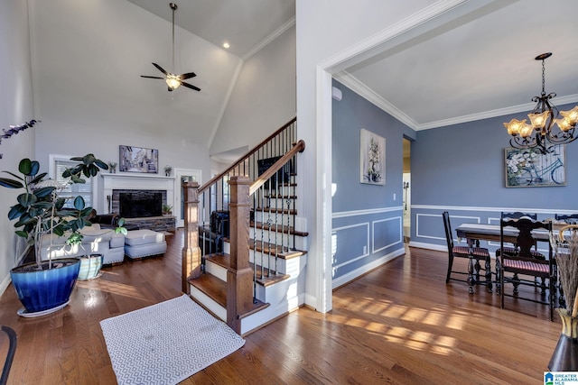 stairway with high vaulted ceiling, ceiling fan with notable chandelier, crown molding, hardwood / wood-style flooring, and a fireplace