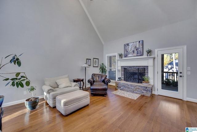 living room with hardwood / wood-style flooring, a stone fireplace, crown molding, and high vaulted ceiling