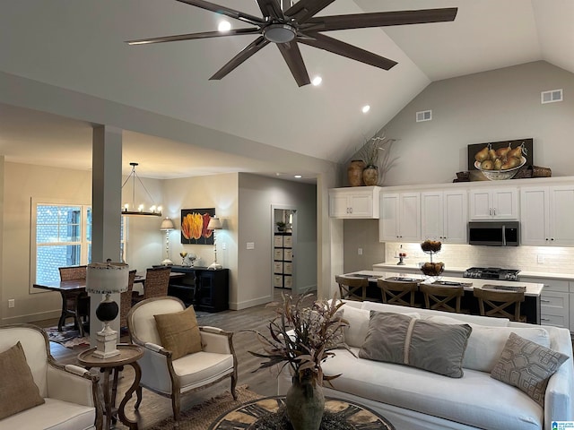 living room featuring ceiling fan with notable chandelier, vaulted ceiling, and light hardwood / wood-style floors