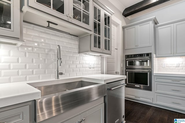 kitchen with dark wood-type flooring, stainless steel appliances, beam ceiling, sink, and tasteful backsplash