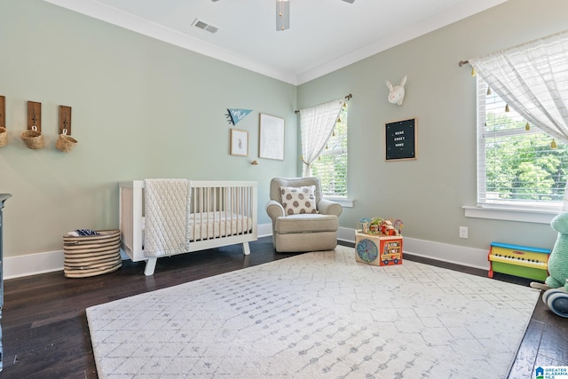 bedroom featuring a nursery area, dark hardwood / wood-style flooring, ceiling fan, and crown molding