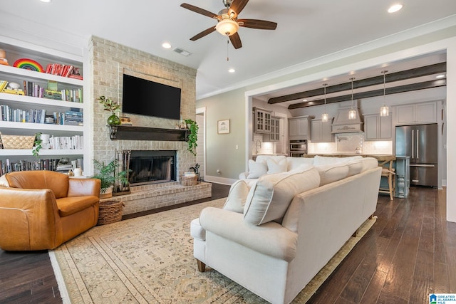 living room with dark hardwood / wood-style floors, ceiling fan, beamed ceiling, a brick fireplace, and ornamental molding