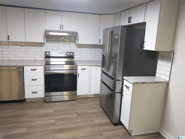 kitchen with light wood-type flooring, under cabinet range hood, backsplash, appliances with stainless steel finishes, and light stone countertops