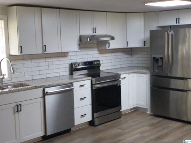 kitchen with stainless steel appliances, backsplash, hardwood / wood-style flooring, light stone countertops, and sink