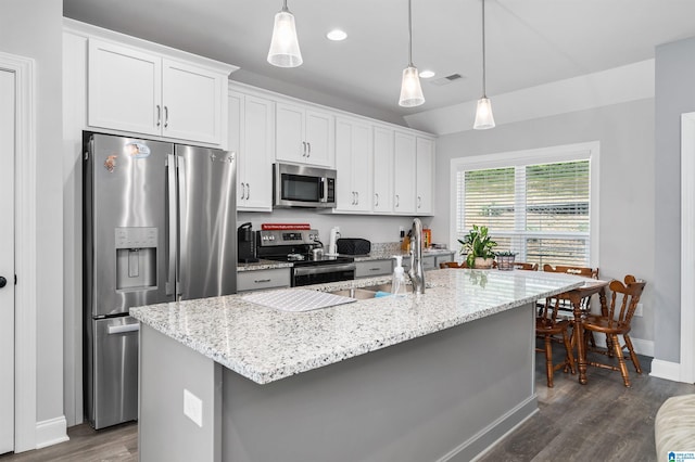 kitchen with stainless steel appliances, white cabinets, a kitchen island with sink, and pendant lighting