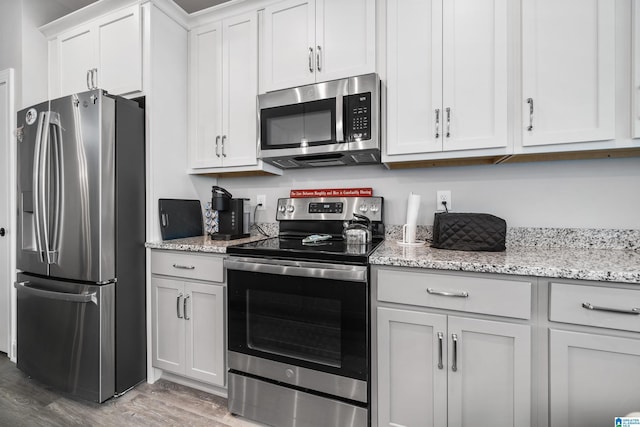 kitchen featuring appliances with stainless steel finishes, white cabinetry, hardwood / wood-style floors, and light stone countertops