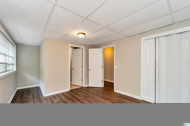 unfurnished bedroom featuring a paneled ceiling, dark hardwood / wood-style floors, and a closet