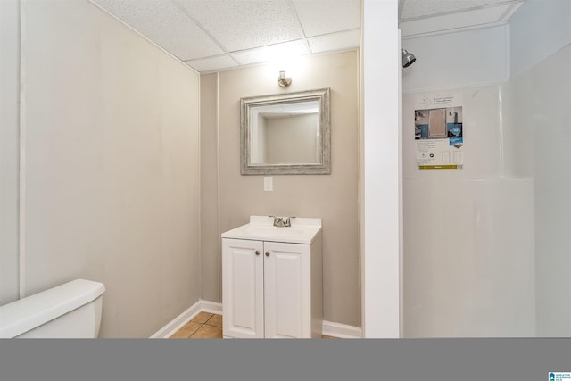 bathroom with tile patterned floors, a drop ceiling, toilet, and vanity