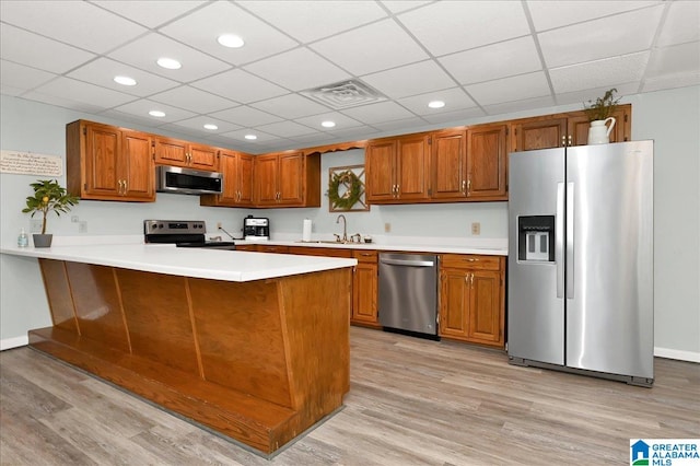 kitchen featuring stainless steel appliances, kitchen peninsula, light wood-type flooring, and sink