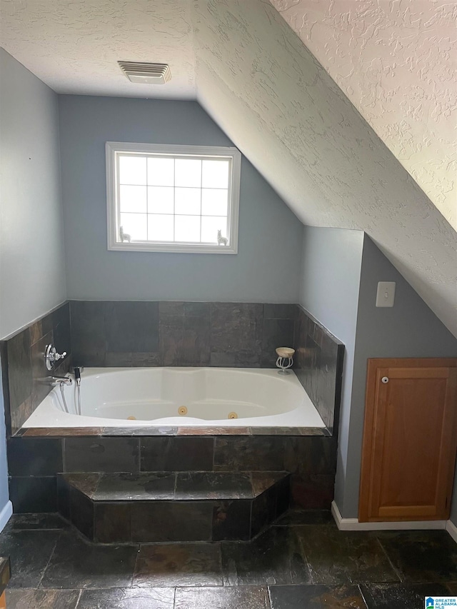 bathroom featuring lofted ceiling, a textured ceiling, and tiled tub