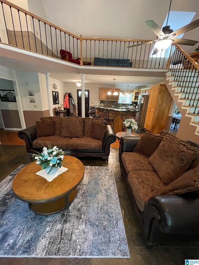 living room featuring a towering ceiling, ceiling fan with notable chandelier, decorative columns, and dark wood-type flooring