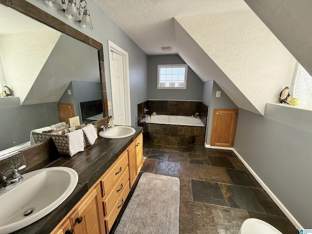 bathroom with a textured ceiling, vanity, lofted ceiling, and tiled tub