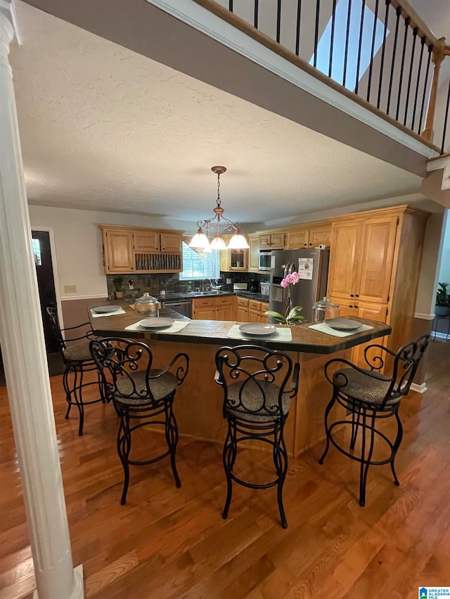 kitchen with kitchen peninsula, stainless steel appliances, sink, light hardwood / wood-style floors, and hanging light fixtures