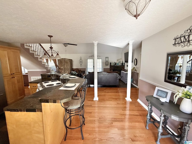 kitchen featuring light hardwood / wood-style flooring, hanging light fixtures, a kitchen breakfast bar, vaulted ceiling, and decorative columns