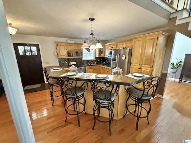 kitchen featuring hanging light fixtures, stainless steel fridge, light hardwood / wood-style floors, a breakfast bar area, and decorative backsplash