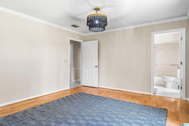 unfurnished bedroom featuring a notable chandelier, hardwood / wood-style floors, crown molding, a textured ceiling, and connected bathroom