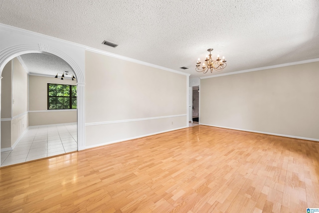 empty room featuring a textured ceiling, light wood-type flooring, a chandelier, and ornamental molding