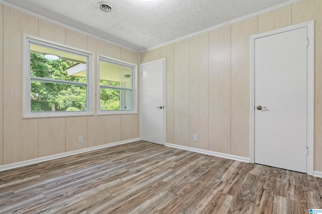 empty room with a textured ceiling, light wood-type flooring, crown molding, and wood walls