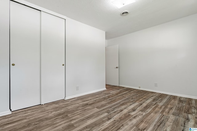 unfurnished bedroom featuring hardwood / wood-style floors, a textured ceiling, and a closet