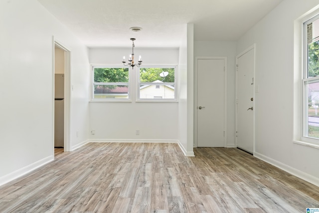 empty room with light wood-type flooring and a notable chandelier