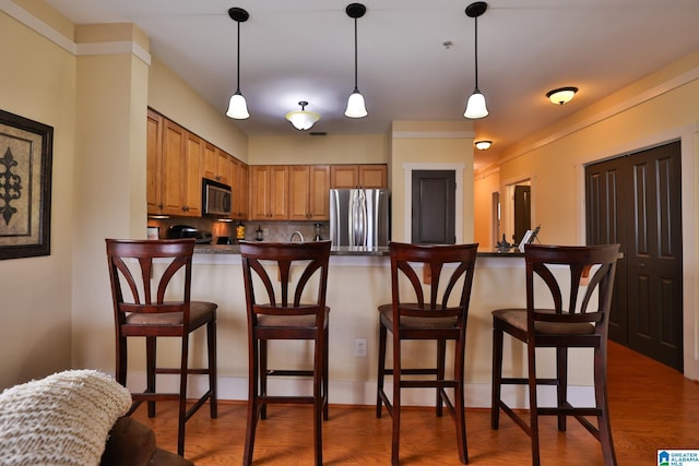 kitchen with dark countertops, brown cabinets, wood finished floors, and freestanding refrigerator