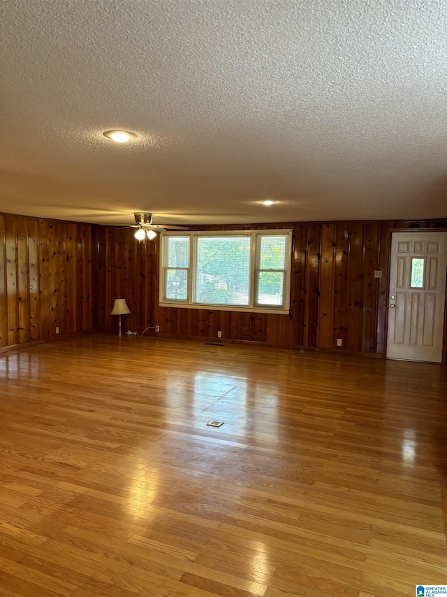 unfurnished living room featuring wood walls, ceiling fan, light hardwood / wood-style floors, and a textured ceiling