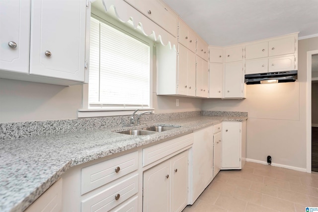 kitchen featuring light stone countertops, ornamental molding, sink, light tile patterned floors, and white cabinets