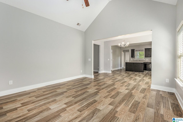 unfurnished living room with hardwood / wood-style flooring, ceiling fan with notable chandelier, and high vaulted ceiling