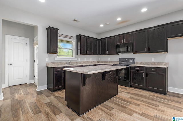 kitchen featuring a center island, black appliances, sink, light hardwood / wood-style flooring, and a breakfast bar area