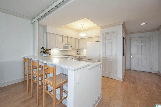 kitchen with a breakfast bar, ornamental molding, light wood-style flooring, a peninsula, and white appliances
