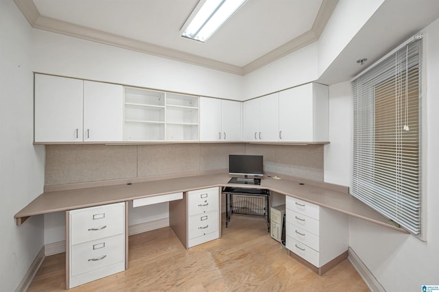 unfurnished office with ornamental molding, baseboards, built in desk, and light wood-type flooring