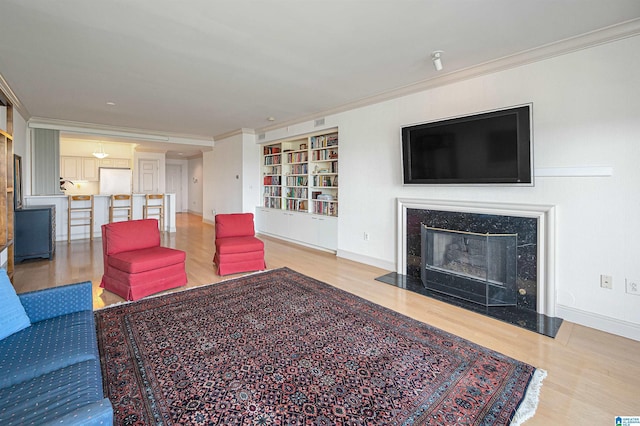 living room with built in shelves, a premium fireplace, wood finished floors, and ornamental molding