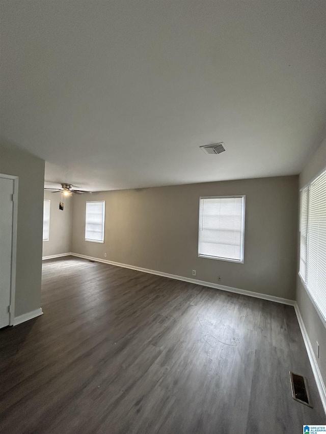 spare room featuring ceiling fan, visible vents, baseboards, and dark wood finished floors