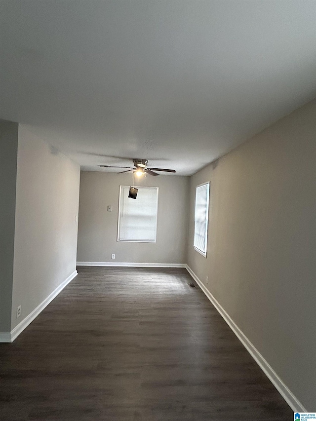 spare room with dark wood-type flooring, a ceiling fan, and baseboards