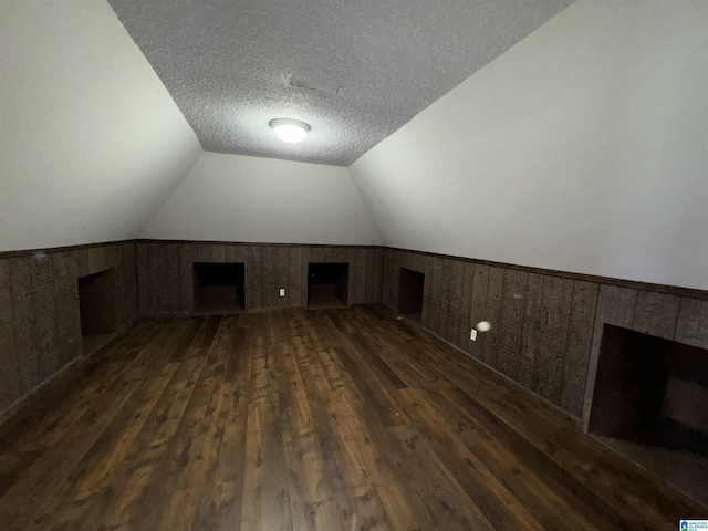 additional living space featuring dark hardwood / wood-style flooring, lofted ceiling, wood walls, and a textured ceiling