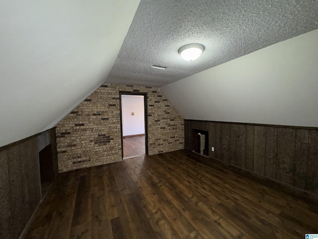 additional living space featuring lofted ceiling, a textured ceiling, brick wall, and dark wood-type flooring