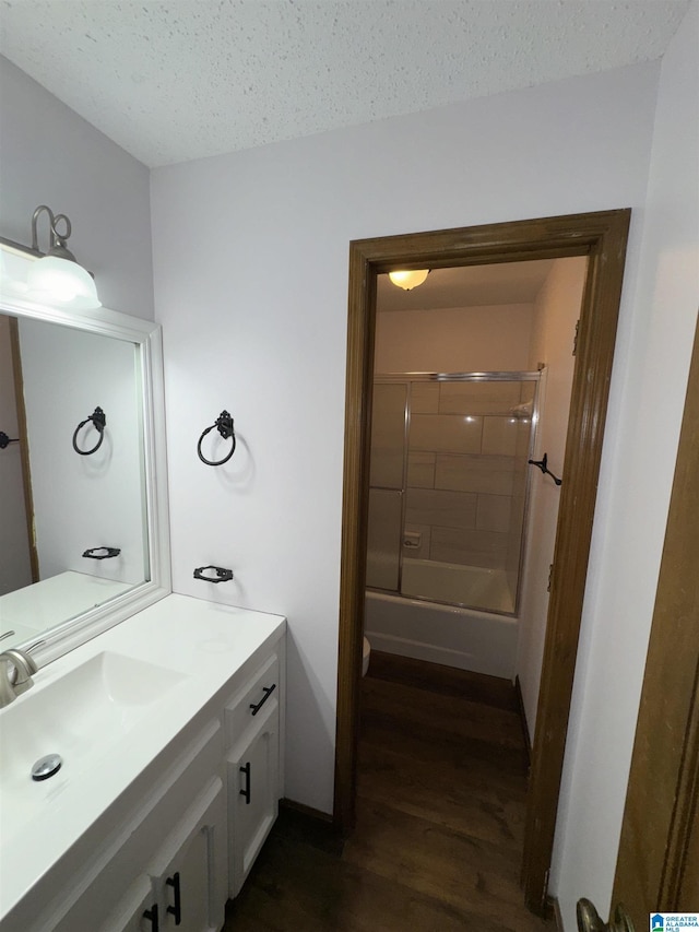 bathroom featuring hardwood / wood-style flooring, vanity, shower / bath combination with glass door, and a textured ceiling