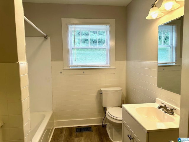 full bathroom featuring shower / bathing tub combination, wood-type flooring, toilet, tile walls, and vanity