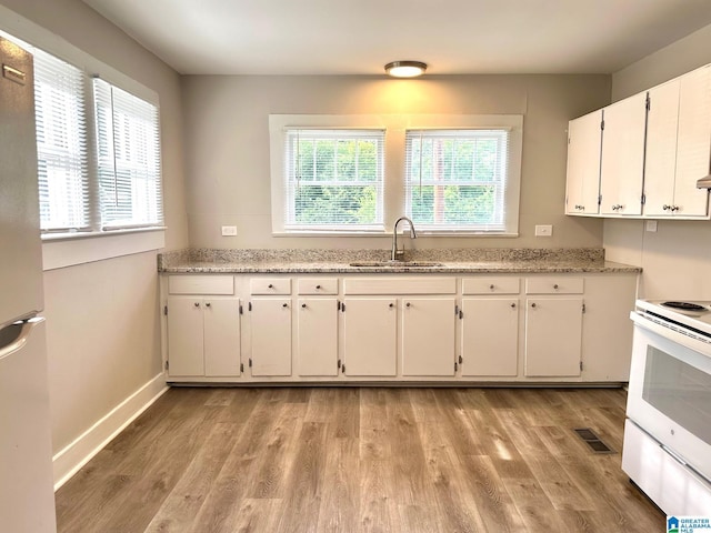 kitchen featuring white electric stove, light stone counters, light wood-type flooring, white cabinets, and sink