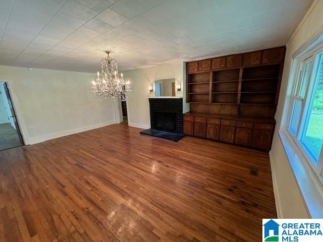 unfurnished living room with dark hardwood / wood-style flooring, built in features, a fireplace, and a chandelier