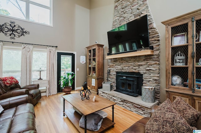 living room with a stone fireplace, light hardwood / wood-style floors, and a high ceiling